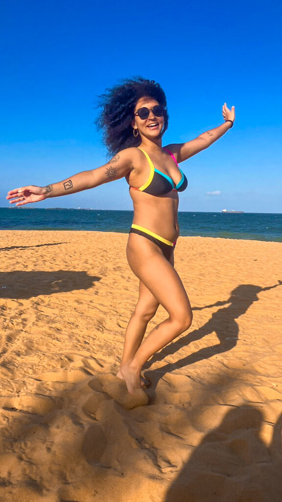 Foto minha sorrindo e de braços abertos na praia