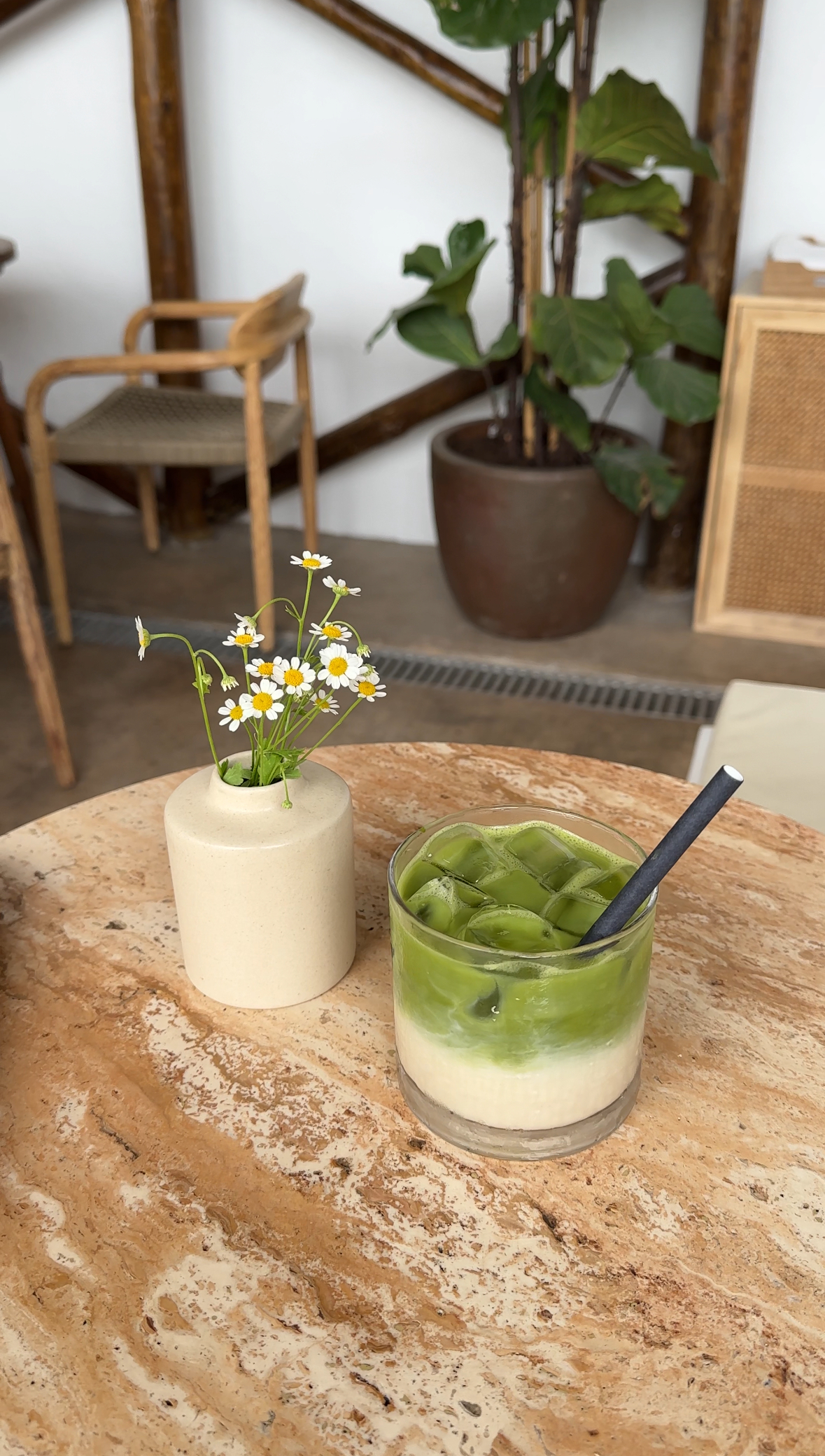 Mesa com um vaso de margaridas e um copo com uma bebida verde ao lado